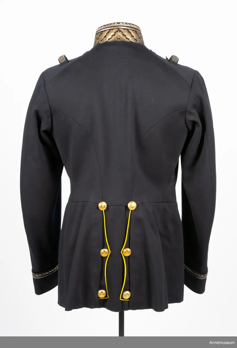 Vapenrock av mörkblått kläde med vitt foder i livet och gult foder i skörtet.
I innerfickan på vänster sida finns en etikett med text: ”G. U. HEURLIN & Cie 6/5 Stockholm 05 Öfverste Brändström”.