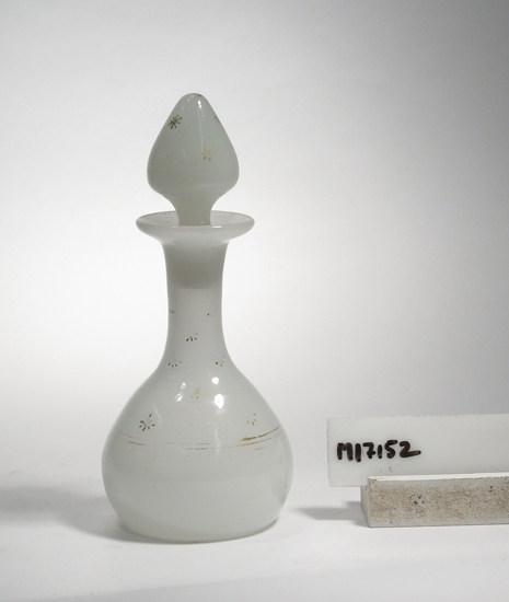 Parfymflacon i vitt opalinglas med målad dekor i guld. Flaskans kropp har formen av en halv ovoid. Halsen lång och rak med utsvängd mynning. Propp med rundad konande knopp.
Inskriven i huvudboken 1962.