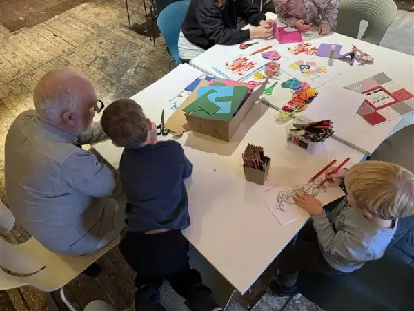 Vi ser et stor bod med flere barn rundt, og en bestefar. De sitter alle og lager julepynt på juleverkstedet vårt