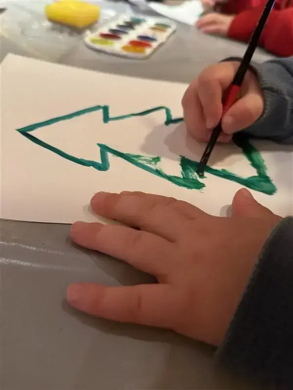 Vi ser en barnehånd som maler et grønt juletre på et hvitt ark