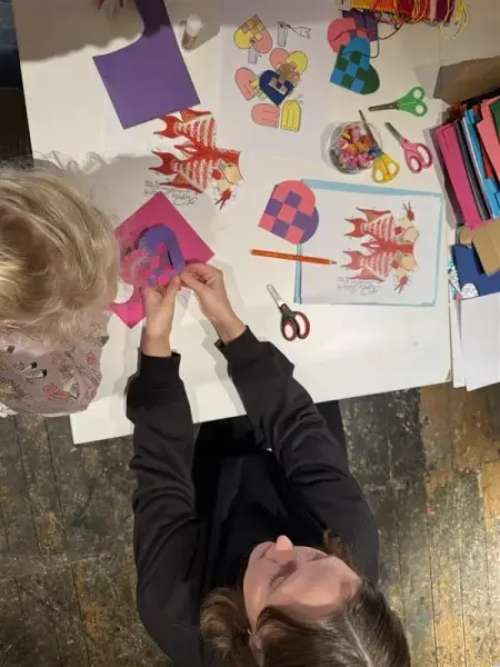 Vi ser i fugleperspektiv ned på et bord hvor barn sitter og lager julekurver i papir, av den typen som henger på julettreet