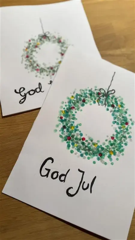 VI ser to fine julekranser malt på hvitt papir, som et enkelt julekort, med påskriften God Jul