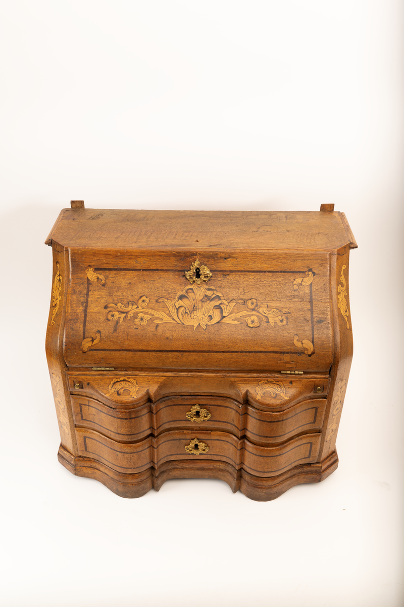 Barneskatoll i rokokkostil med separat overskap og underskap samt felles nøkkel til begge deler. Underskap med kraftig buet og profilert front, to skuffer samt nedfellbart pultlokk med hylle-, skap- og skuffseksjon innenfor. Overskap med to rette dører og kraftig profilert, delvis gjennombrutt gesims. Både over- og underskapet rikt dekorert med intarsia av høy kvalitet med rocailler, skjell, konturlinjer og blomsterornamentikk. Dekorative skilt av messing rundt alle nøkkelhull. Initialer og årstall på skapdør bak pultlokk. Skatollet står på to lave føtter.

A: underskap
B: nøkkel
C: overskap