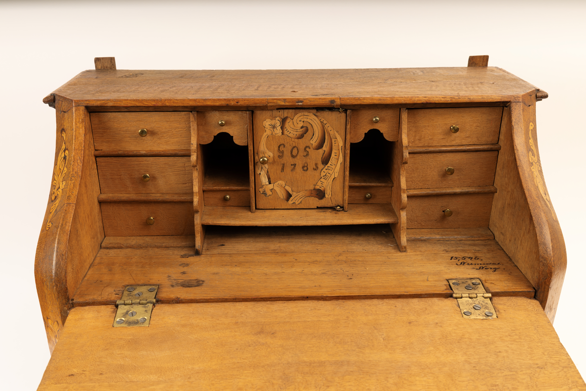 Barneskatoll i rokokkostil med separat overskap og underskap samt felles nøkkel til begge deler. Underskap med kraftig buet og profilert front, to skuffer samt nedfellbart pultlokk med hylle-, skap- og skuffseksjon innenfor. Overskap med to rette dører og kraftig profilert, delvis gjennombrutt gesims. Både over- og underskapet rikt dekorert med intarsia av høy kvalitet med rocailler, skjell, konturlinjer og blomsterornamentikk. Dekorative skilt av messing rundt alle nøkkelhull. Initialer og årstall på skapdør bak pultlokk. Skatollet står på to lave føtter.

A: underskap
B: nøkkel
C: overskap