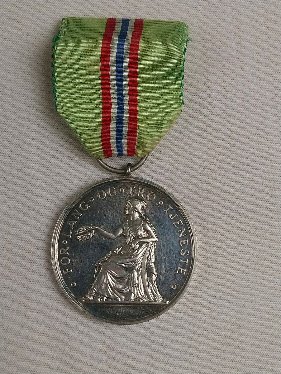 Medalje fra "Det kongelige selskap for Norges vel" for lang og tro tjeneste. Medaljen ligger i en svarte eske med hvit filt inni, merket David-Andersen, Oslo.