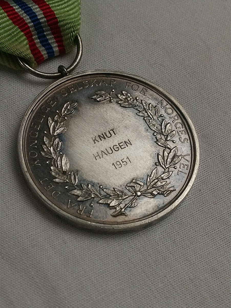 Medalje fra "Det kongelige selskap for Norges vel" for lang og tro tjeneste. Medaljen ligger i en svarte eske med hvit filt inni, merket David-Andersen, Oslo.