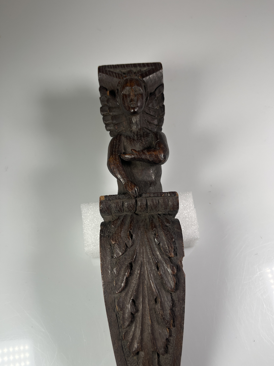 Överkroppen av en ängel på ett pelarformigt postament med bladdekor framtill.
Funktion: Avsedd att hängas på vägg