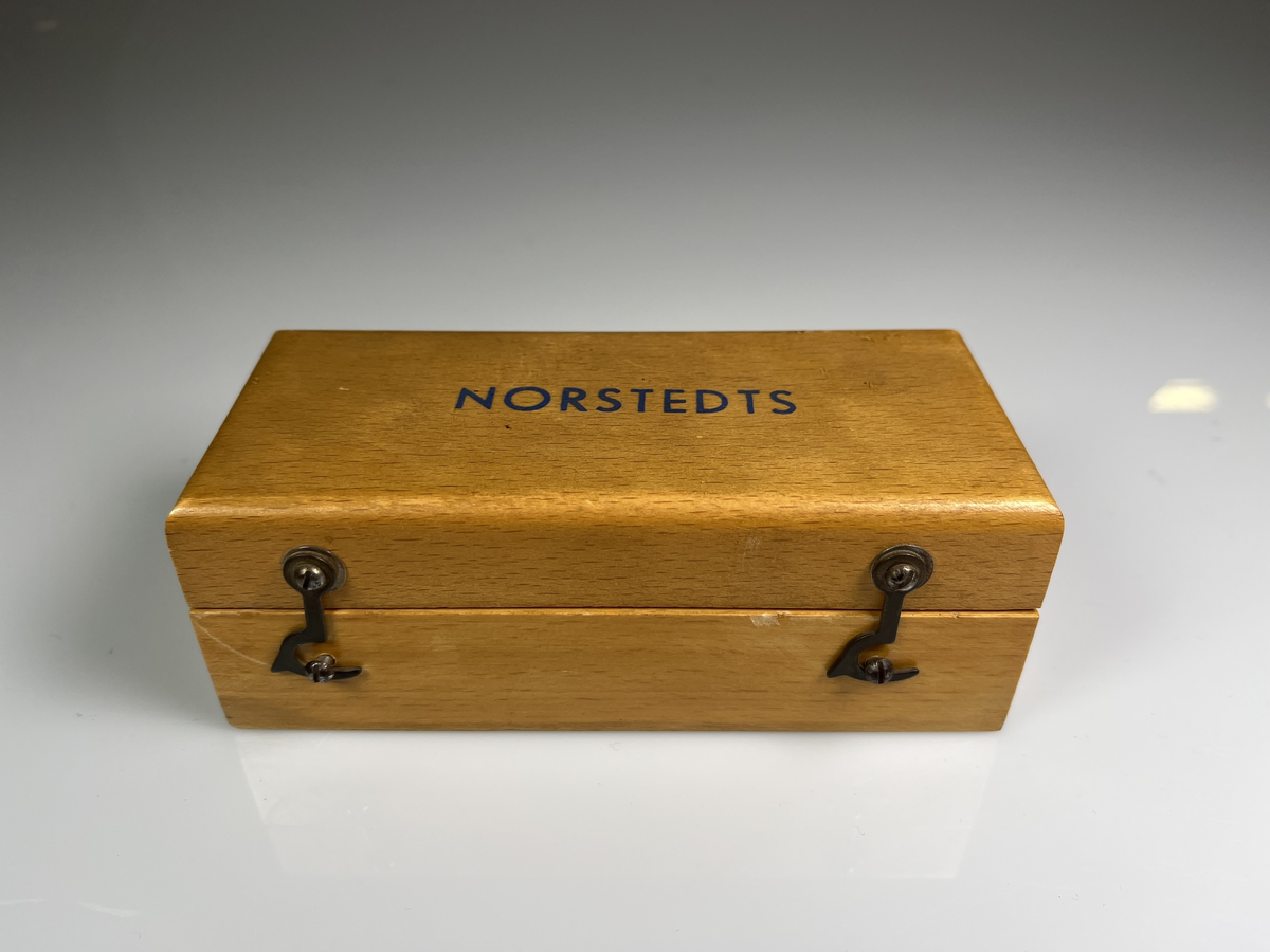 Rektangulär trälåda som låses med små hakar. Text på locket: Norstedts.
Lådan innehåller vikter (1-, 2-, 4-, 5-, 10-, 20- (2st), 50- och 100-gram) av mässing. Även milligramsvikter av små mässingbleck, dessa täcks av en plexiglasskiva. Det finns också en pincett av mässing.
Liknar de lådor som användes i skolan när man skulle lära sig om vikt.

Från Arne Ekströms Handelsmuseum.