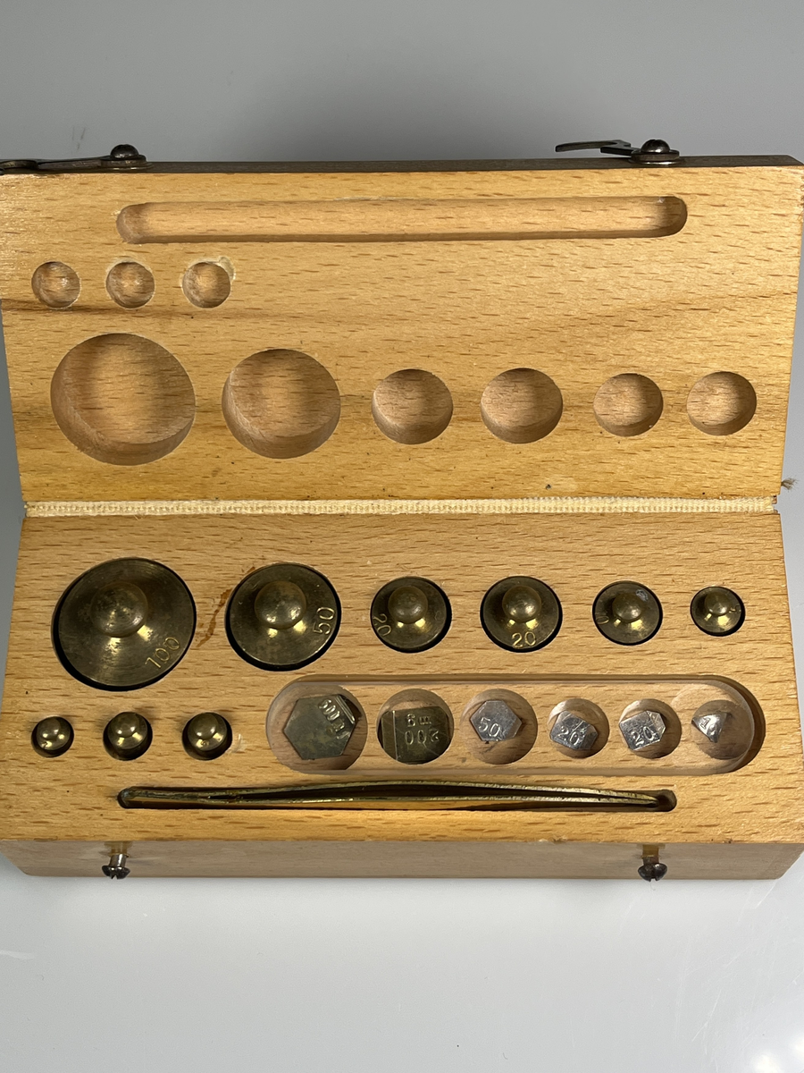 Rektangulär trälåda som låses med små hakar. Text på locket: Norstedts.
Lådan innehåller vikter (1-, 2-, 4-, 5-, 10-, 20- (2st), 50- och 100-gram) av mässing. Även milligramsvikter av små mässingbleck, dessa täcks av en plexiglasskiva. Det finns också en pincett av mässing.
Liknar de lådor som användes i skolan när man skulle lära sig om vikt.

Från Arne Ekströms Handelsmuseum.