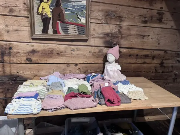 FIne babyklær på et bord og en del av en utstillingsdukke med klær og lure på. 