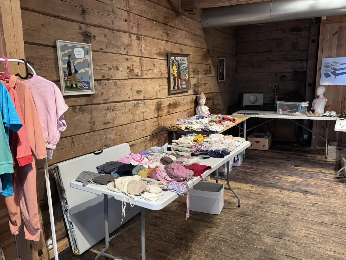 Vi e rinne i sjøboden og ser bord med barneklær, en del av tilbudet Åpen dør om onsdagene