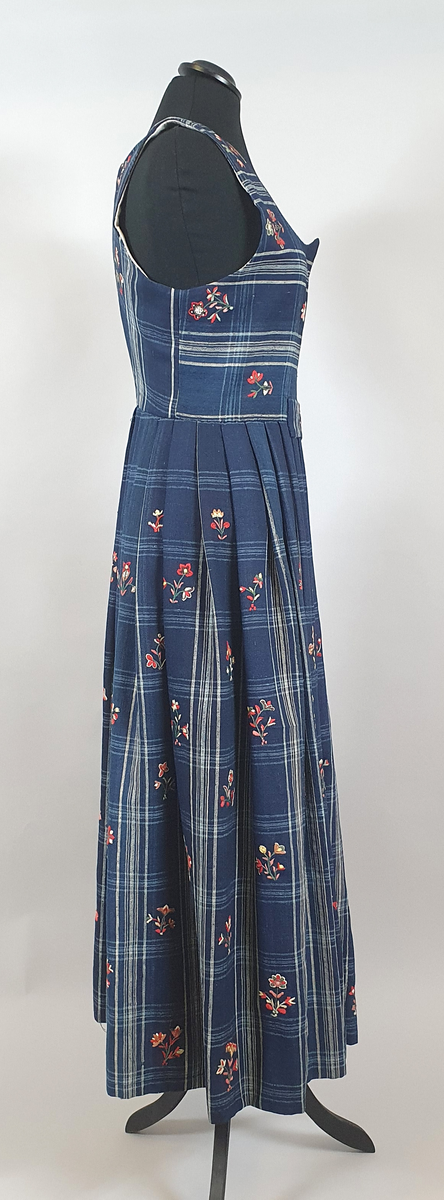 Blå stakk med liv. Hvite og lyseblå smale ruter på mørkeblå bunn, med broderte blomster spredt utover hele stakken og livet. Alle blomstene er ulike, brodert på frihånd. Livet er sydd på stakken i senere tid, og er fôret med hvitt bomullsstoff. Blå skoning av bomull på innsiden av skjørtekanten.