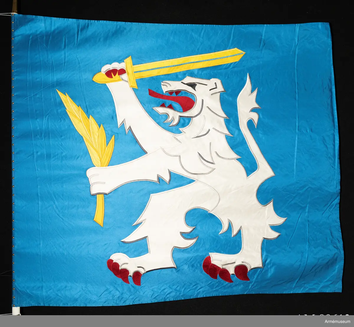 Blå fana med ett vitt lejon med röda och gula detaljer.

Fanduken är tillverkad av blått så kallat fansiden, kypertvävt, med applikationsbroderi i form av ett relativt kantigt framställt vitt lejon hållande ett gult svärd och en gul olivkvist med löv. Lejonet har röda klor och röd tunga.

Fanan är handbroderad med plattsöm, schattérsöm och applikationsbroderi. De gula detaljerna består av applicerat gult fansiden i två olika nyanser medan de röda detaljerna är broderade.

Fanstången är slät och vitmålad. Den nedre halvan mäter 118 cm varav doppskon är ca 11 cm lång och kromad, och skarvdelen av mässing är ca 18 cm.

Fanduken är märkt IB och GF 2007, troligen brodörerna Gertie Frid och Inger Broström.