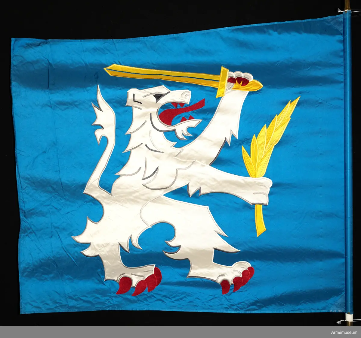 Blå fana med ett vitt lejon med röda och gula detaljer.

Fanduken är tillverkad av blått så kallat fansiden, kypertvävt, med applikationsbroderi i form av ett relativt kantigt framställt vitt lejon hållande ett gult svärd och en gul olivkvist med löv. Lejonet har röda klor och röd tunga.

Fanan är handbroderad med plattsöm, schattérsöm och applikationsbroderi. De gula detaljerna består av applicerat gult fansiden i två olika nyanser medan de röda detaljerna är broderade.

Fanstången är slät och vitmålad. Den nedre halvan mäter 118 cm varav doppskon är ca 11 cm lång och kromad, och skarvdelen av mässing är ca 18 cm.

Fanduken är märkt IB och GF 2007, troligen brodörerna Gertie Frid och Inger Broström.