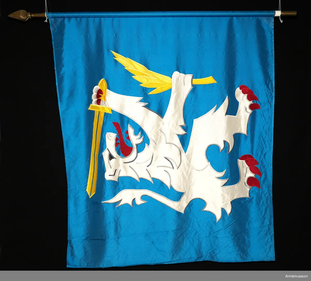 Blå fana med ett vitt lejon med röda och gula detaljer.

Fanduken är tillverkad av blått så kallat fansiden, kypertvävt, med applikationsbroderi i form av ett relativt kantigt framställt vitt lejon hållande ett gult svärd och en gul olivkvist med löv. Lejonet har röda klor och röd tunga.

Fanan är handbroderad med plattsöm, schattérsöm och applikationsbroderi. De gula detaljerna består av applicerat gult fansiden i två olika nyanser medan de röda detaljerna är broderade.

Fanstången är slät och vitmålad. Den nedre halvan mäter 118 cm varav doppskon är ca 11 cm lång och kromad, och skarvdelen av mässing är ca 18 cm.

Fanduken är märkt IB och GF 2007, troligen brodörerna Gertie Frid och Inger Broström.