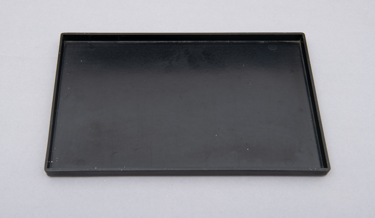 Myntkassett i svart bakelitt, inneholdende 8 behoholdere sortet på de ulike valørene 1, 2, 5, 10, 25 og 50 øre. 1 og 5 kroner. Hvit skrift.
