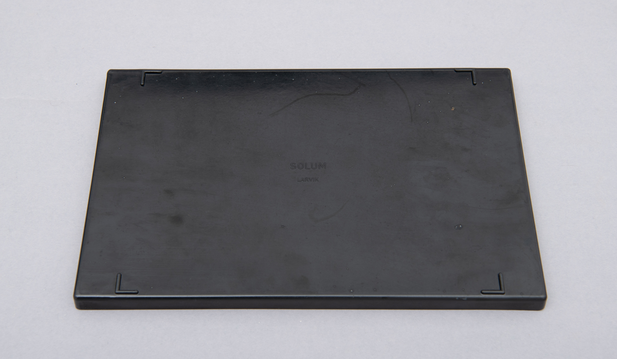 Myntkassett i svart bakelitt, inneholdende 8 behoholdere sortet på de ulike valørene 1, 2, 5, 10, 25 og 50 øre. 1 og 5 kroner. Hvit skrift.
