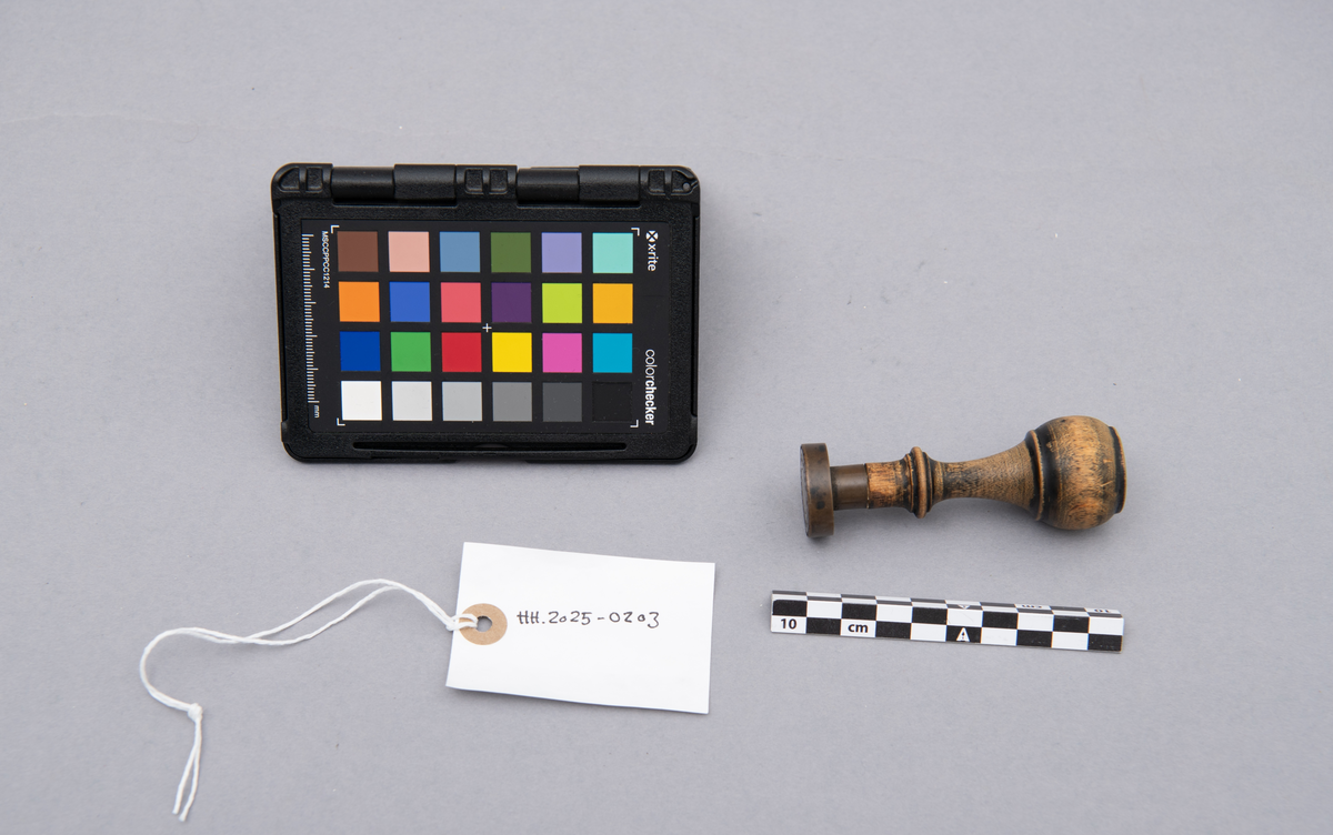 Rundt stempel i messing, med dreiet treskaft.