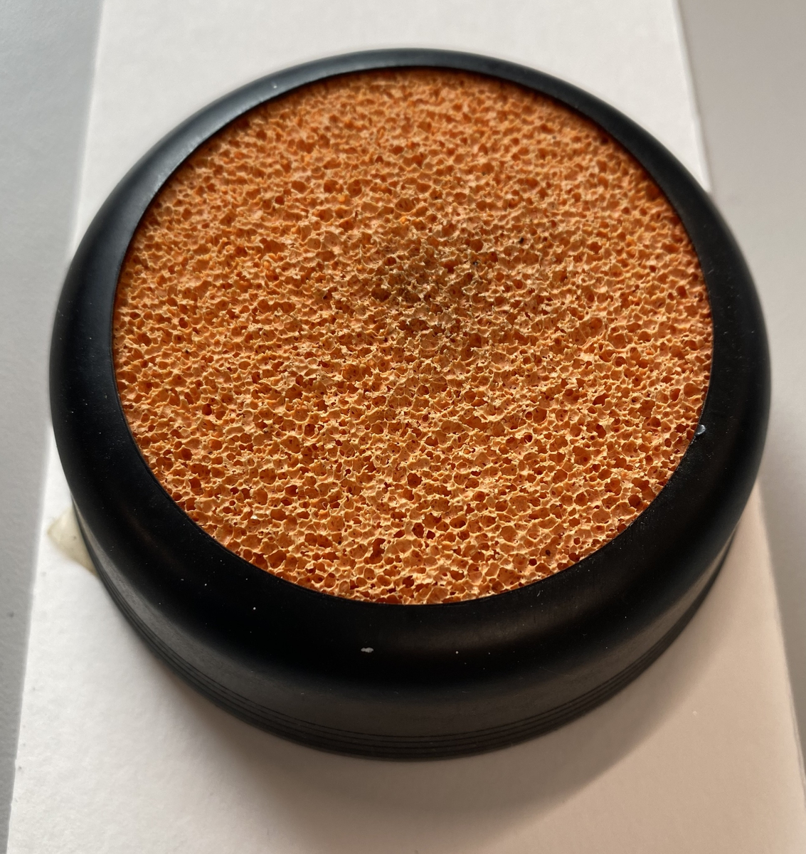 Svamp for fukt av fingre. Holder i svart plast. Oransje svamp av gummi.