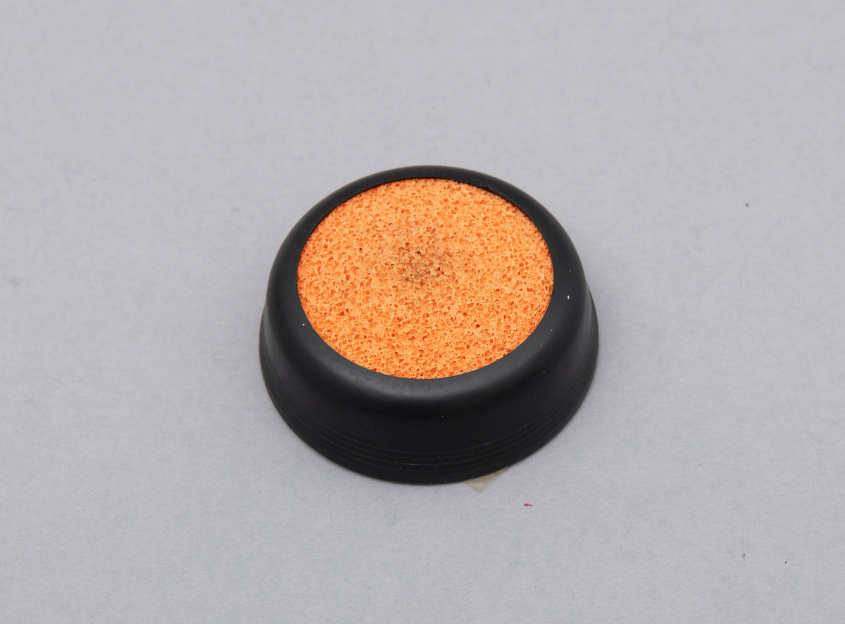 Svamp for fukt av fingre. Holder i svart plast. Oransje svamp av gummi.