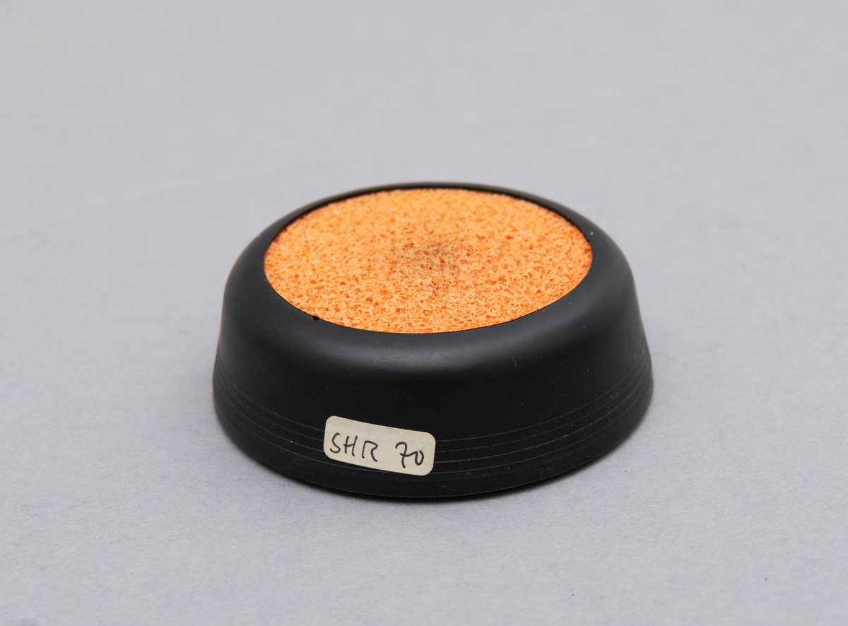 Svamp for fukt av fingre. Holder i svart plast. Oransje svamp av gummi.