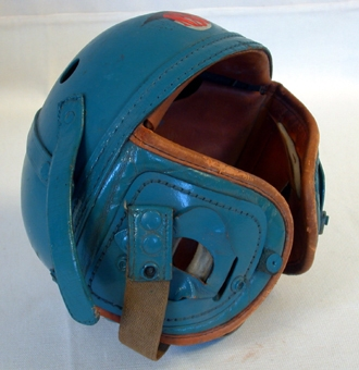 Ytterhölje bestående av en halvklotsformad kupa av turkosfärgat, hårt konstmaterial på insidan klädd med läder som på baksidan är stoppad med filt. På två motsatta sidor av kupans nederkant sitter två stycken, även de på utsidan klädda med det hårda konstmaterialet, på insidan med det stoppade lädret.  När kupan sätts på huvudet blir dessa som skydd för öron och kinder. På kupans baksida ett liknande stycke som skydd för nacke. På kupans ovansida, tio stycken ventilationshål vardera med diameter 20 mm. På framsidan står bokstäverna NSU i rött på en svart-vit bakgrund. Med ett ca 370 mm långt resårband med knappar i vardera ände som fästs på hjälmen, hålls hjälmen fast på huvudet. På insidan står stämplat: "Wilson Ath. Goods (oläsligt) Co. Chicago, Ill. 7 1/4.