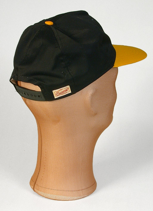 Keps i svart tyg. Skärm i hård papp klädd med klargult tyg på ovansidan och limegrönt tyg på undersidan. Klargul klädd knapp på kepsens topp. Mitt fram en cirkel med gult lagerbladsliknande mönster i hästskoform,  tryck med text  UIF samt hund eller varg siluett. Kepsen fodrad med vitt tyg mitt fram, vitt svettband. Mitt bak byglar för storleksändring i plast,