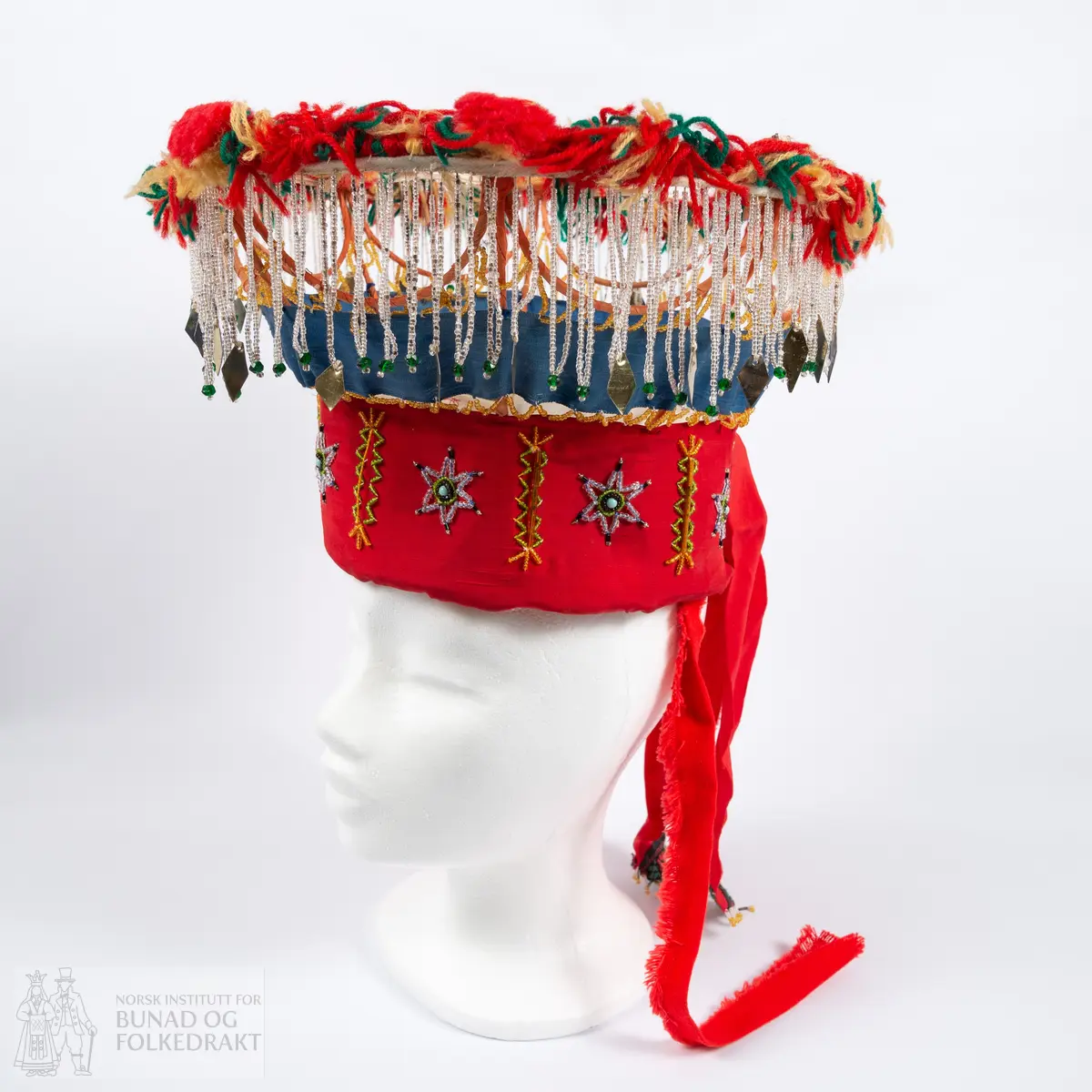 Krone til jonsokbryllup. Perlekrone med trøsk av papp. 
Utsida er dekka med et rødt syntetisk stoff. Innsida er dekka med ubleka bomullslerret, og er polstret med bomullsvatt. Det røde stoffet er perlebrodert, vekselsvis med stjerner og striper. Øverst midt bak er det sydd på to brede, røde bånd av samme stoff som det er festa rundt trøsken.
En liten spiss med mønstrete ullstoff med innvevd blomstermønster er sydd på i enden på hver av båndene, disse er kanta med perler.
Knytebånd av grovt, rødt bomullsbånd. Over trøsken sitter en smal bord med gule perler, deretter er festa et blått syntetisk bånd.
Begge deler støtta opp av spiler, som er dekka med et syntetisk oransje stoff. Øverst er spilene dekka med et hvitt skråbånd. Til øverste kant er festa dusker av ullgarn i rødt, gult og grønt.
Til øverste kant er det festa noen perlefrynser, noen er dekorert med en større rombeforma metallbit i enden, mens andre har en større grønn perle.
Eier har fått opplyst at dette skal stamme fra en gammel lampeskjerm. Krona har også en rad gule perler rett over det blå båndet.
All synlig søm er gjort for hånd.
Produsent laget utstyret sammen med sine barn ca. 1910-1920. Trolig brukt til 1970-åra.