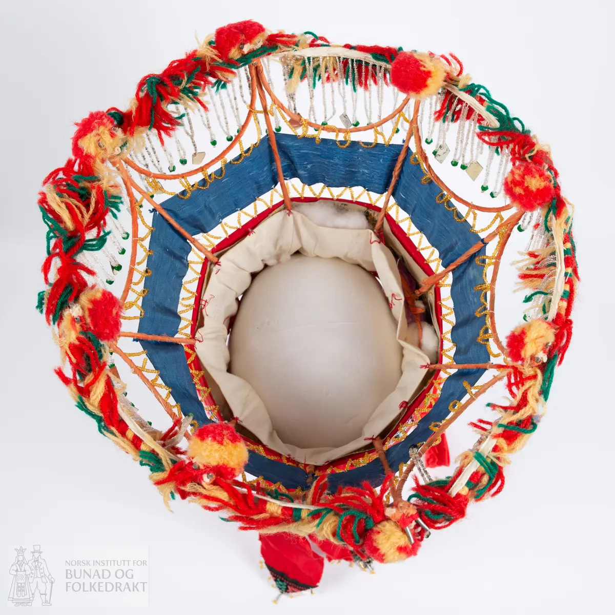 Krone til jonsokbryllup. Perlekrone med trøsk av papp. 
Utsida er dekka med et rødt syntetisk stoff. Innsida er dekka med ubleka bomullslerret, og er polstret med bomullsvatt. Det røde stoffet er perlebrodert, vekselsvis med stjerner og striper. Øverst midt bak er det sydd på to brede, røde bånd av samme stoff som det er festa rundt trøsken.
En liten spiss med mønstrete ullstoff med innvevd blomstermønster er sydd på i enden på hver av båndene, disse er kanta med perler.
Knytebånd av grovt, rødt bomullsbånd. Over trøsken sitter en smal bord med gule perler, deretter er festa et blått syntetisk bånd.
Begge deler støtta opp av spiler, som er dekka med et syntetisk oransje stoff. Øverst er spilene dekka med et hvitt skråbånd. Til øverste kant er festa dusker av ullgarn i rødt, gult og grønt.
Til øverste kant er det festa noen perlefrynser, noen er dekorert med en større rombeforma metallbit i enden, mens andre har en større grønn perle.
Eier har fått opplyst at dette skal stamme fra en gammel lampeskjerm. Krona har også en rad gule perler rett over det blå båndet.
All synlig søm er gjort for hånd.
Produsent laget utstyret sammen med sine barn ca. 1910-1920. Trolig brukt til 1970-åra.