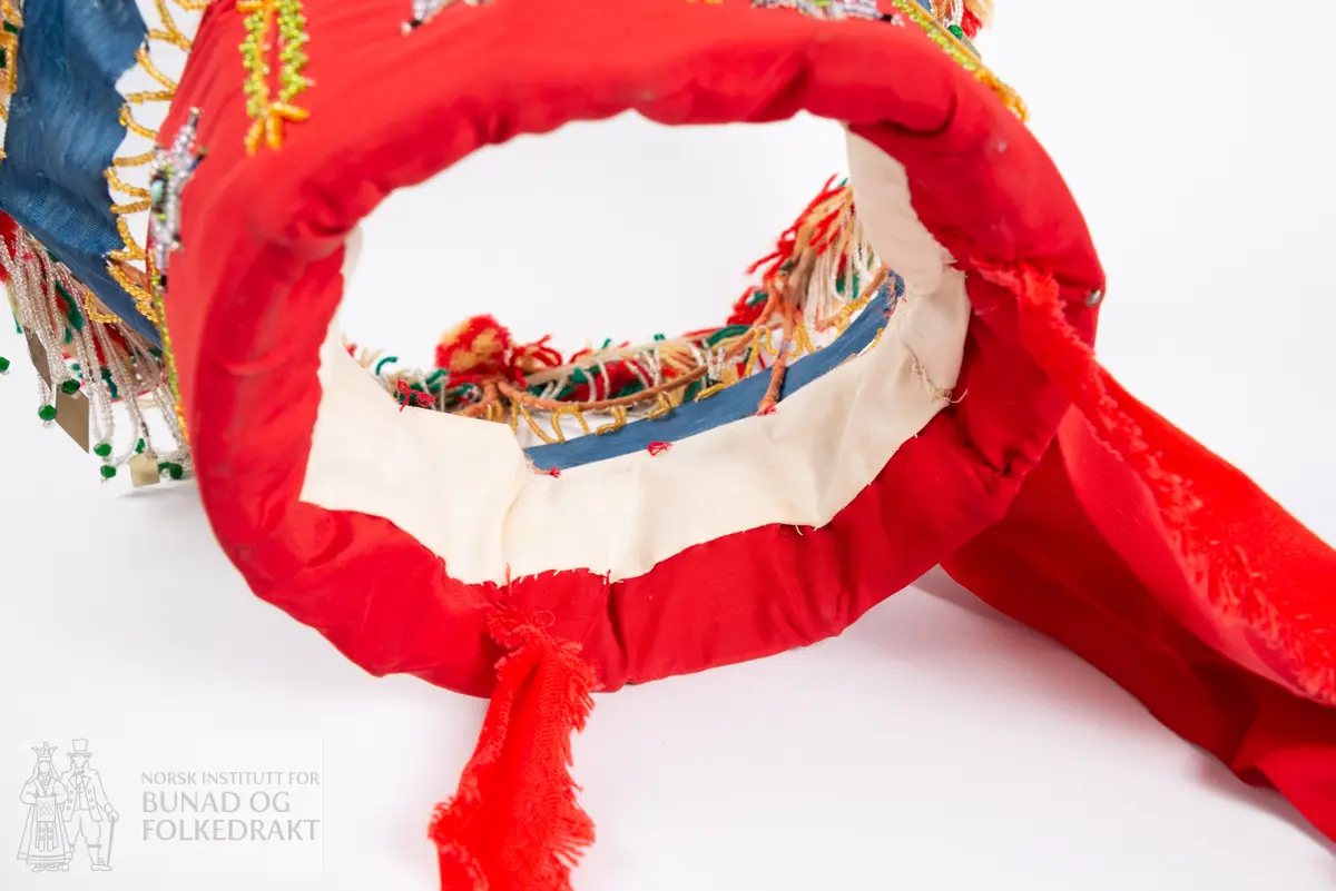 Krone til jonsokbryllup. Perlekrone med trøsk av papp. 
Utsida er dekka med et rødt syntetisk stoff. Innsida er dekka med ubleka bomullslerret, og er polstret med bomullsvatt. Det røde stoffet er perlebrodert, vekselsvis med stjerner og striper. Øverst midt bak er det sydd på to brede, røde bånd av samme stoff som det er festa rundt trøsken.
En liten spiss med mønstrete ullstoff med innvevd blomstermønster er sydd på i enden på hver av båndene, disse er kanta med perler.
Knytebånd av grovt, rødt bomullsbånd. Over trøsken sitter en smal bord med gule perler, deretter er festa et blått syntetisk bånd.
Begge deler støtta opp av spiler, som er dekka med et syntetisk oransje stoff. Øverst er spilene dekka med et hvitt skråbånd. Til øverste kant er festa dusker av ullgarn i rødt, gult og grønt.
Til øverste kant er det festa noen perlefrynser, noen er dekorert med en større rombeforma metallbit i enden, mens andre har en større grønn perle.
Eier har fått opplyst at dette skal stamme fra en gammel lampeskjerm. Krona har også en rad gule perler rett over det blå båndet.
All synlig søm er gjort for hånd.
Produsent laget utstyret sammen med sine barn ca. 1910-1920. Trolig brukt til 1970-åra.