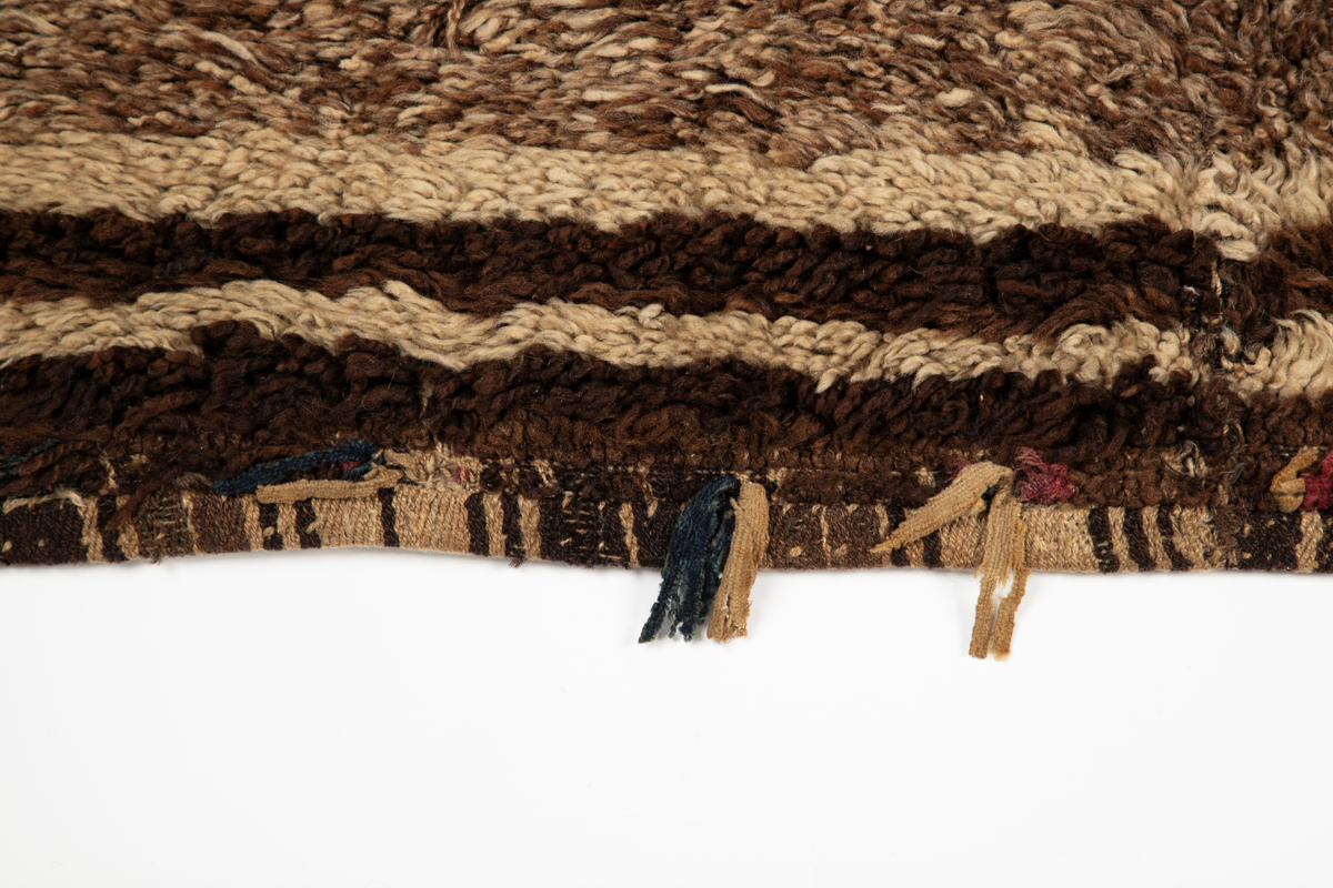 Håndlaget rye i ull, flossteknikk, Bunnen består av treskaftet kyper (stoff vevd med et mønster av skrå linjer), sydd sammen av tre bredder. Fargene er hvitt, sauesvart, brunt og brunmelert. Glattsiden er stripet på langs. På flossiden er det i den ene enden hvite og brune tverrstriper og et felt med brune ruter på hvit bunn (sjakkbrettruter). Mellom disse felt et brunmelert felt hvori initialer og årstall: "A S P  1816". Resten er brunmelert. Stoffdusker øverst i rød, blå og sauehvit ull.