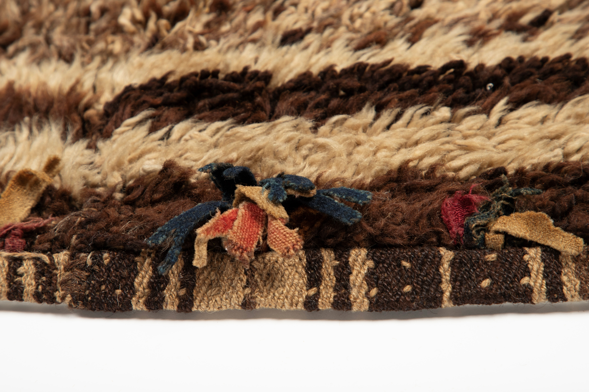 Håndlaget rye i ull, flossteknikk, Bunnen består av treskaftet kyper (stoff vevd med et mønster av skrå linjer), sydd sammen av tre bredder. Fargene er hvitt, sauesvart, brunt og brunmelert. Glattsiden er stripet på langs. På flossiden er det i den ene enden hvite og brune tverrstriper og et felt med brune ruter på hvit bunn (sjakkbrettruter). Mellom disse felt et brunmelert felt hvori initialer og årstall: "A S P  1816". Resten er brunmelert. Stoffdusker øverst i rød, blå og sauehvit ull.