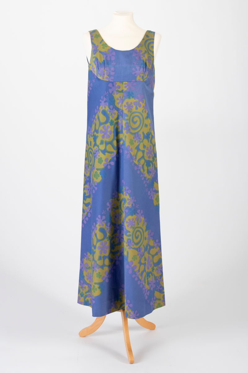 Lang, ermeløs kjole i blålilla mønstertrykket, satengvevd bomullsstoff. Kjolen er lett innsvinget med høyt liv og utskrådd skjørt. Lav, rundet utringning foran og v-formet utringning bak. Kjolen har mørkeblått silkefôr og glidelås i ryggen.