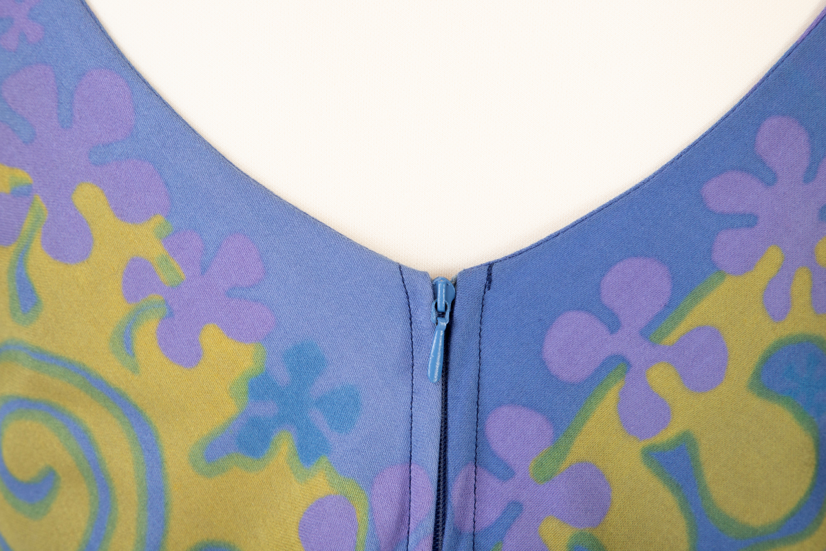 Lang, ermeløs kjole i blålilla mønstertrykket, satengvevd bomullsstoff. Kjolen er lett innsvinget med høyt liv og utskrådd skjørt. Lav, rundet utringning foran og v-formet utringning bak. Kjolen har mørkeblått silkefôr og glidelås i ryggen.