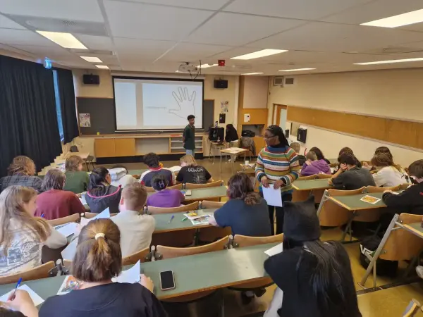 Et klasserom med studenter fotografert bakfra mot en skjerm med tegning av en hånd.