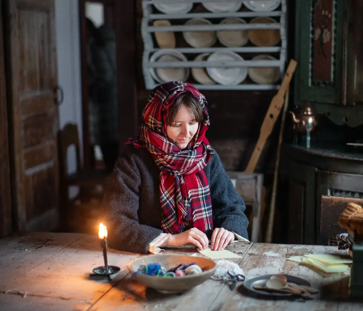 Kvinna i sjal sitter i gammal köksmijö från 1800-talet och gör vaxljus