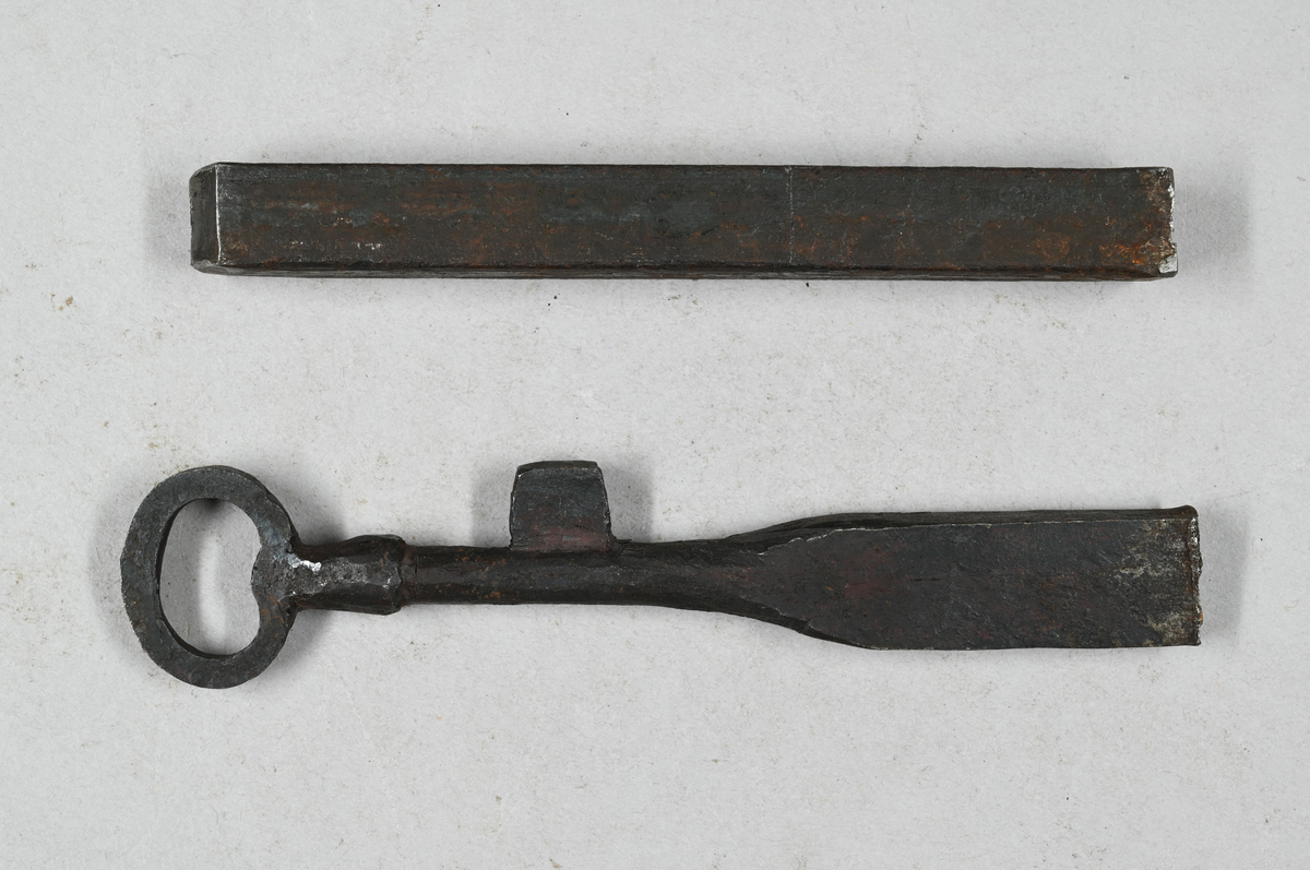 Två prover på nyckelämnen av järn. Märkning på ena provet med stämpel: "Högfors". Ett av proverna visar smidning av nyckelämne. Båda proverna från Högfors. Tillhörande lapp med samma notering.