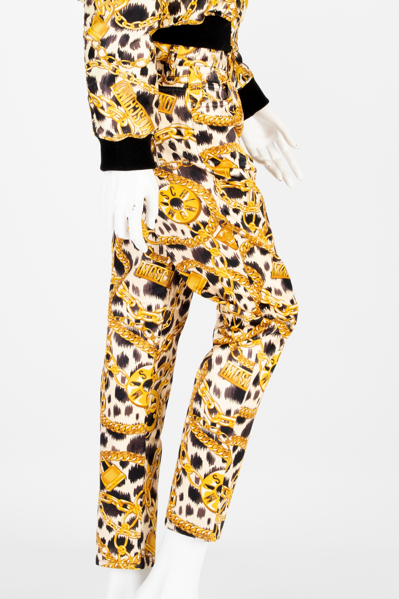 Lavtsittende, slank damebukse av ganske blankt materiale, med påtrykt mønster i form av tettstilte, gullfargede lenker, hengelåser og bærbare radioer/spillere, noen av dem påtrykt navnet Moschino, mot en bakgrunn med dyremønster. Gylf lukket med glidelås, linning med beltestoler og lukket med knapp og knapphull. Jeanslomme på hvert forstykke, den høyre har i tillegg "pengelomme". Alle lommer på forsiden er forsterket med metallnagler og har bomullsfôr. Baksiden har bærestykke opp mot linningen og påsydde, åpne lommer på hvert bakstykke.