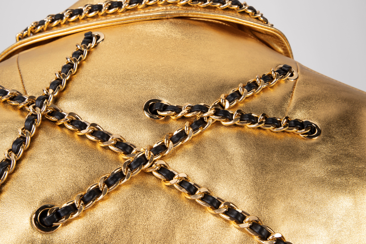 Kort skinnjakke med passepoilerte lommer med gullfarget glidelås og liten lomme med klaff, krage og slag. Lukkes med glidelås midt foran. Tosøms erme med smalt glidelås ved håndleddet. Jakken er dekorert med gullfarget kjetting med skinnsnor smettet inn, tredd gjennom gullfargede maljer på plagget. Dekoren er på krage, forstykke, ermer og bakstykke. Belte med gullfarget spenne i jakkens nederkant.