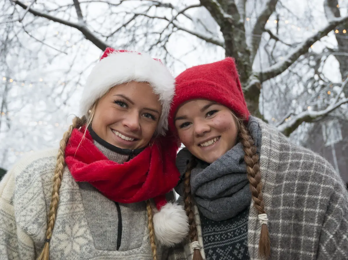 To jenter står kledd med nisseluer og smiler