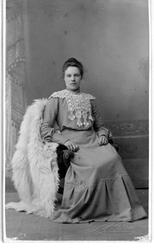 Portrett i helfigur av en kvinne i fotsid kjole, sittende i 