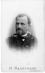 Brystbilde av mann med helskjegg, iført mørk jakke og skjort