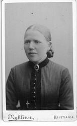 Brystbilde av kvinne med stramt hår i midtskill, mørk kneppe