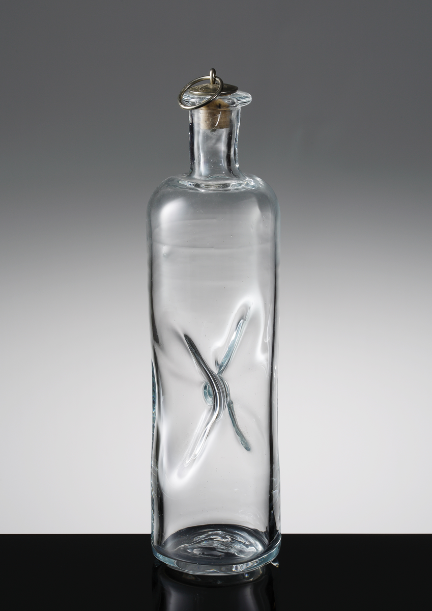 Flaska med två instick som möter varandra i mitten på kroppen. Driven hals med äldre ringförsedd propp med Frederik IX's präglade monogram under en krona och årtalet 1967.