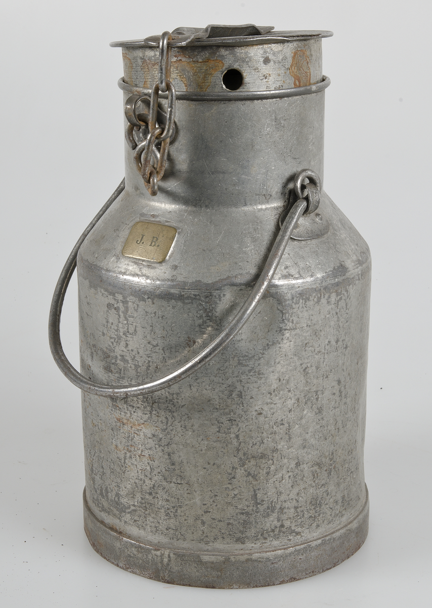 Mjölkhämtare av förzinkad järmplåt, flaska med lock fäst med kedja, hänkel. På skuldran en liten mässingsbricka med initialerna J. B.
Rostfläckar.
