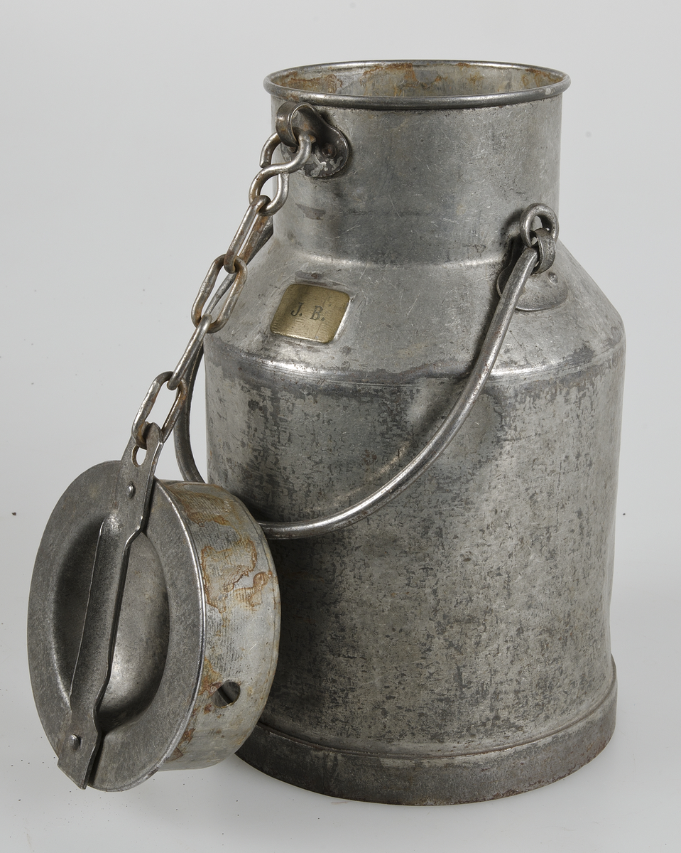 Mjölkhämtare av förzinkad järmplåt, flaska med lock fäst med kedja, hänkel. På skuldran en liten mässingsbricka med initialerna J. B.
Rostfläckar.