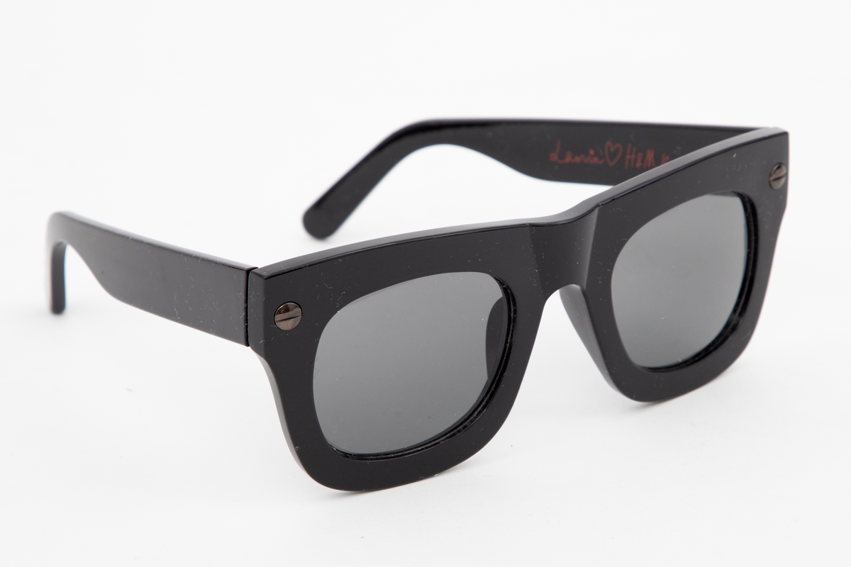 Solbriller i svart plast med svarte glass, stor og avrundet i formen.