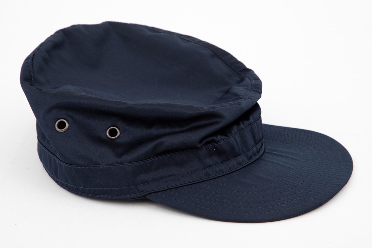 Høy kaps med stiv brem/skygge foran, såkalt "negl". Bremmen er avstivet innvendig, mellom ytterside og innside, og stukket med seks parallelle sømmer. Pullen er forsterket i nederkant med påsydd belegg utvendig, også det med stikninger. Innvendig et "svettebånd" av samme materiale, "vattert" og stukket. Pullen er sylindrisk og det innfelte toppstykket helt flatt. Hatten er ufôret og luftes gjennom to maljehull i hver side.