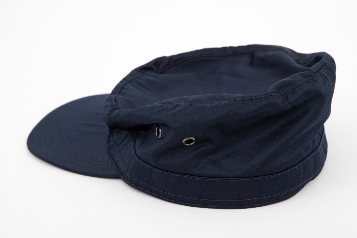 Høy kaps med stiv brem/skygge foran, såkalt "negl". Bremmen er avstivet innvendig, mellom ytterside og innside, og stukket med seks parallelle sømmer. Pullen er forsterket i nederkant med påsydd belegg utvendig, også det med stikninger. Innvendig et "svettebånd" av samme materiale, "vattert" og stukket. Pullen er sylindrisk og det innfelte toppstykket helt flatt. Hatten er ufôret og luftes gjennom to maljehull i hver side.