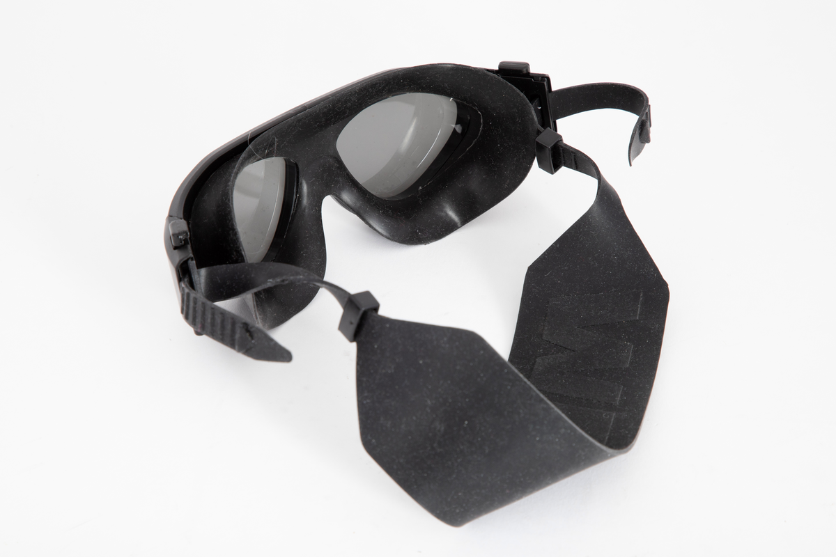 Støpt innfatning med innfelte, utstående glass av trekantet form. Ekstra ledd på hver side, med fjærbelastet feste for gummi- eller silikonstroppen som holder brillen fast mot hodet. Den 5 cm brede stroppen er avsmalnet til 1 cm i hver ende, med en rekke hakk/trinn ytterst, slik at den kan forkortes eller forlenges ved justering av hakkene i festet. Tappene kan tres gjennom en smygstol på hver side. Brillene holdes tett inntil ansiktet, ved hjelp av en myk "mansjett" av silikon eller gummi omkring øynene.